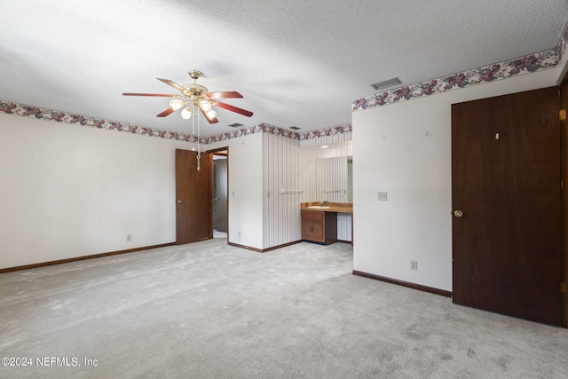 unfurnished bedroom with ceiling fan, light carpet, ensuite bath, and a textured ceiling