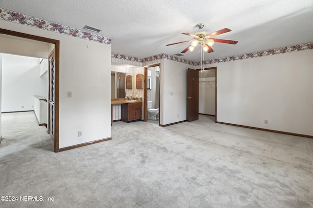 unfurnished bedroom with ensuite bathroom, ceiling fan, light carpet, a textured ceiling, and a closet