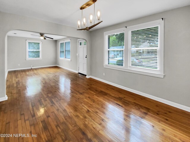 empty room featuring a wealth of natural light, ceiling fan with notable chandelier, and dark wood-type flooring