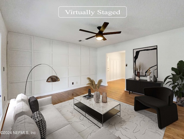 living room featuring ceiling fan, light hardwood / wood-style flooring, and a textured ceiling