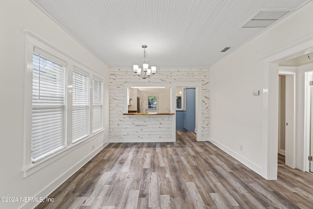 unfurnished dining area featuring visible vents, a notable chandelier, baseboards, and wood finished floors