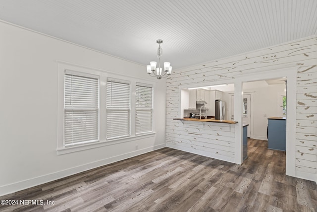 unfurnished dining area featuring dark wood-style floors, a sink, a notable chandelier, and baseboards