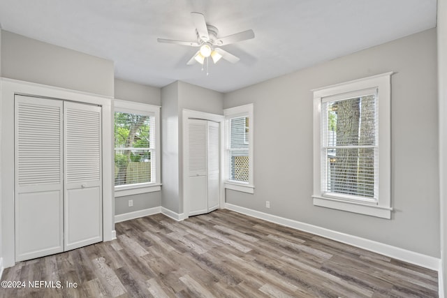 unfurnished bedroom featuring baseboards, multiple windows, light wood-style flooring, and multiple closets