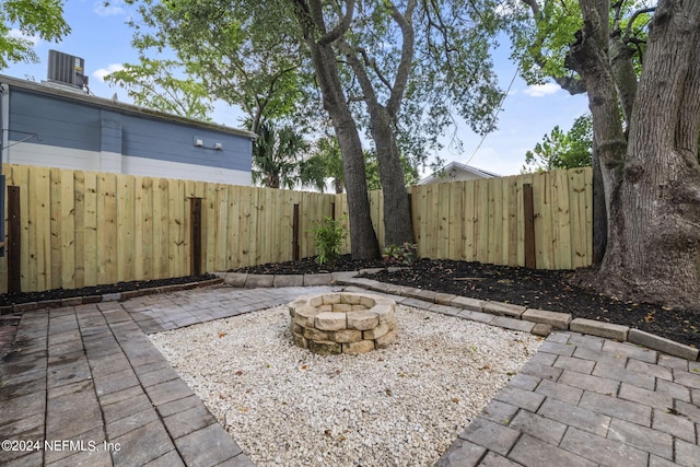 view of yard with central air condition unit, a patio area, a fenced backyard, and a fire pit