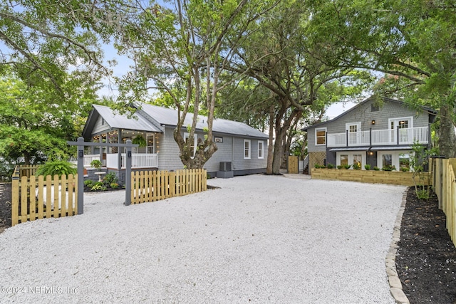 back of property with covered porch, driveway, a fenced front yard, and a balcony