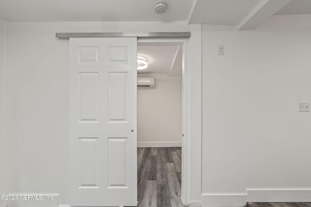 hall featuring a wall mounted air conditioner, wood finished floors, and baseboards