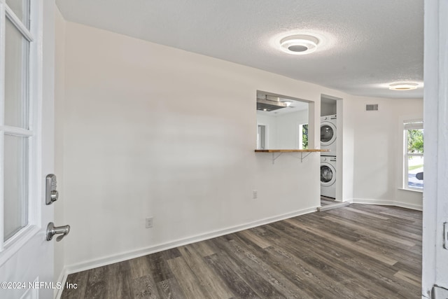 laundry area with dark wood finished floors, stacked washer and dryer, visible vents, a textured ceiling, and laundry area