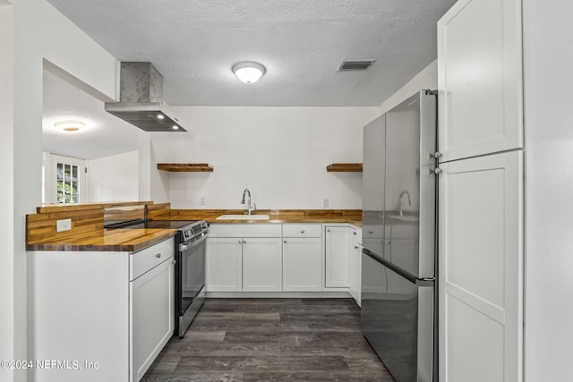 kitchen with butcher block counters, a sink, white cabinetry, wall chimney range hood, and appliances with stainless steel finishes