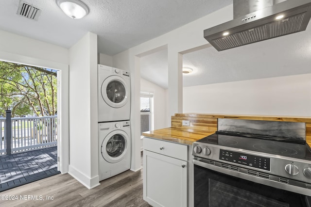 kitchen with stainless steel electric stove, stacked washer / drying machine, visible vents, white cabinetry, and wall chimney exhaust hood