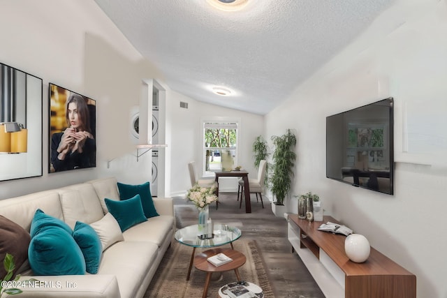 living room featuring visible vents, stacked washer and clothes dryer, lofted ceiling, dark wood-type flooring, and a textured ceiling