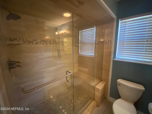 bathroom featuring tile patterned flooring, toilet, and a shower with door