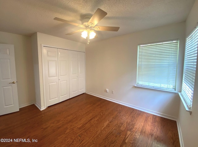 unfurnished bedroom featuring ceiling fan, multiple windows, dark wood-type flooring, and a closet