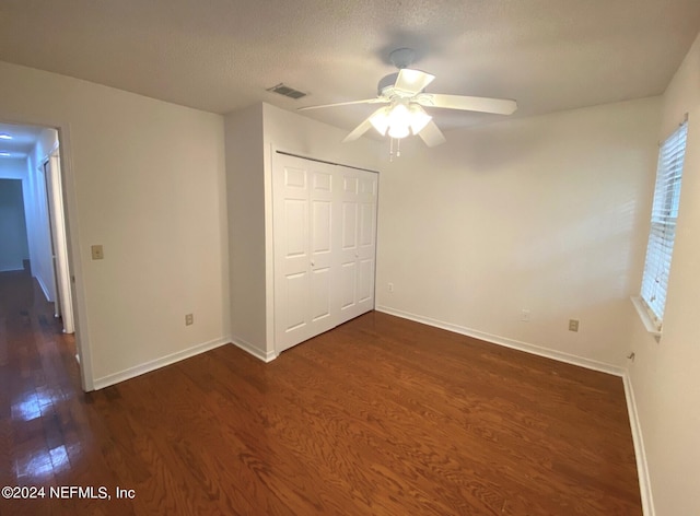 unfurnished bedroom with ceiling fan, a textured ceiling, multiple windows, dark hardwood / wood-style flooring, and a closet