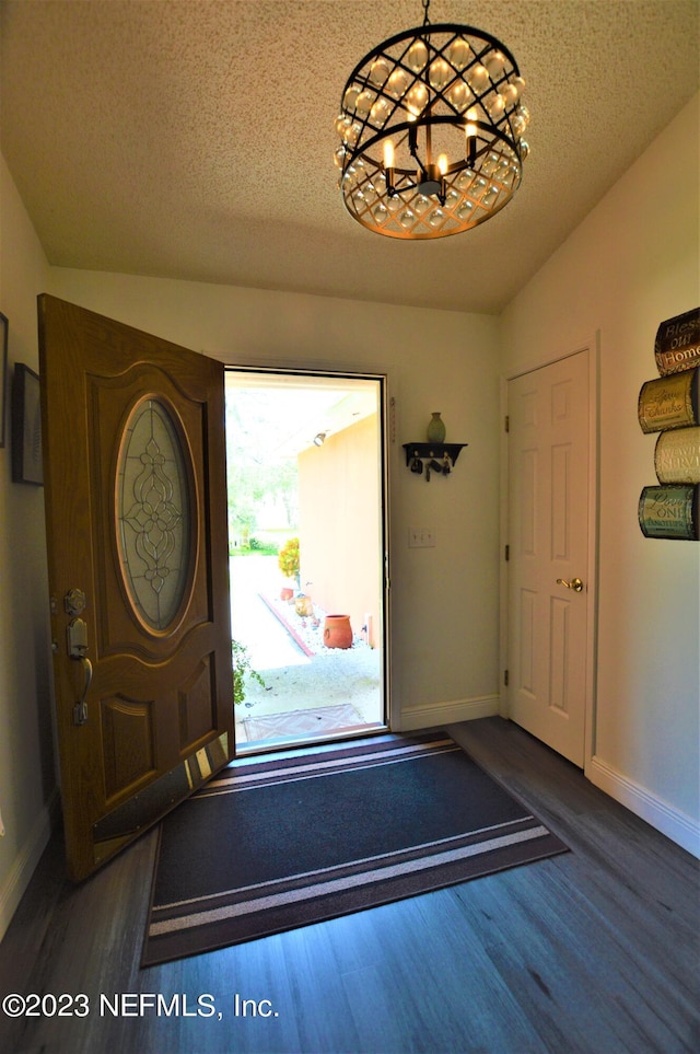 foyer with lofted ceiling, a chandelier, dark wood-type flooring, and a textured ceiling