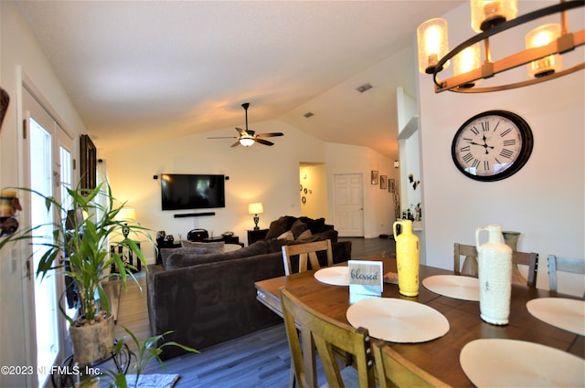 dining space with ceiling fan with notable chandelier, lofted ceiling, and dark wood-type flooring