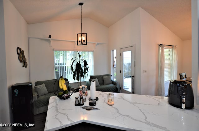 interior space featuring a healthy amount of sunlight, light stone counters, lofted ceiling, and hanging light fixtures