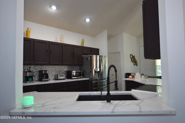 kitchen with appliances with stainless steel finishes, tasteful backsplash, light stone counters, and sink