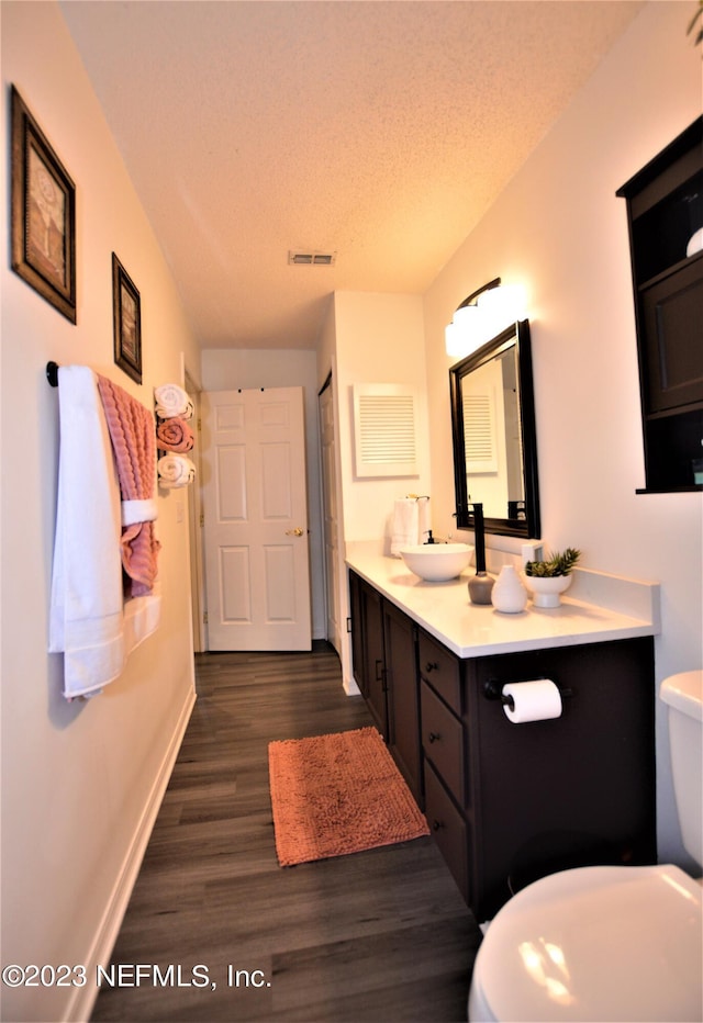 bathroom with hardwood / wood-style floors, vanity, toilet, and a textured ceiling