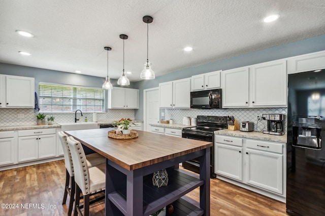 kitchen with black appliances, decorative backsplash, white cabinets, and hardwood / wood-style floors