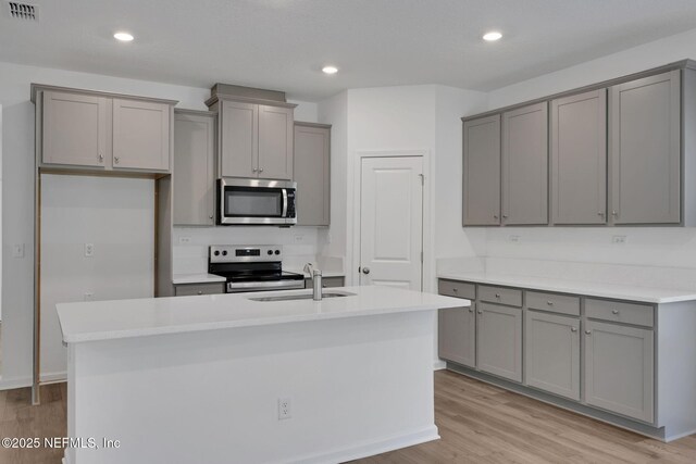 kitchen featuring a kitchen island with sink, stainless steel appliances, and gray cabinetry