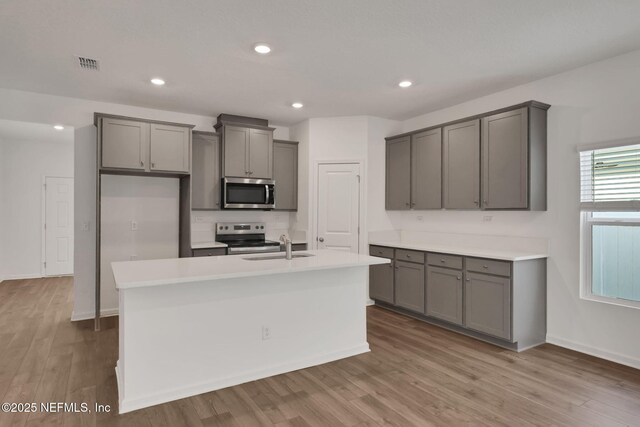 kitchen featuring sink, gray cabinetry, a center island with sink, light wood-type flooring, and appliances with stainless steel finishes