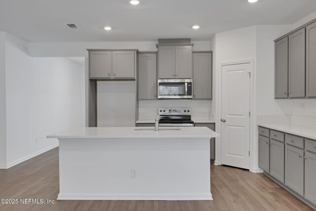 kitchen with stainless steel appliances, gray cabinets, and a center island with sink