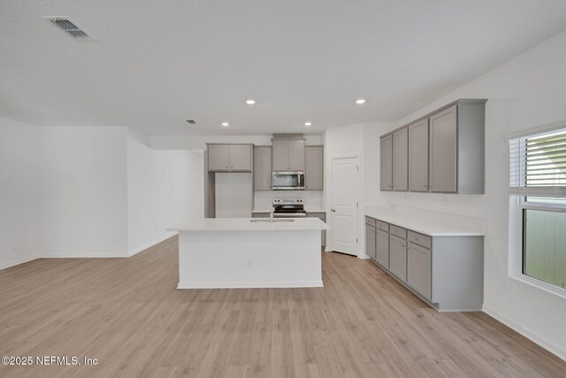 kitchen with gray cabinets, appliances with stainless steel finishes, sink, a center island with sink, and light wood-type flooring