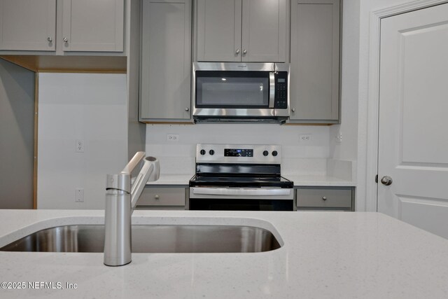 kitchen with stainless steel appliances, gray cabinets, and light stone countertops