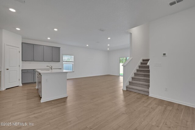 kitchen with a healthy amount of sunlight, light wood-type flooring, a center island with sink, and gray cabinetry