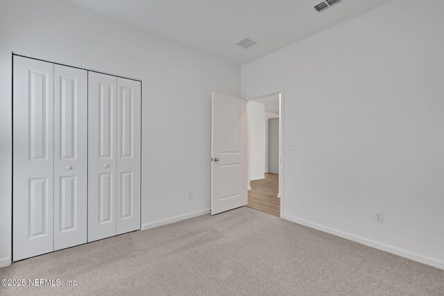 unfurnished bedroom with light colored carpet and a closet