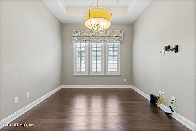 spare room with a tray ceiling, dark hardwood / wood-style flooring, and an inviting chandelier