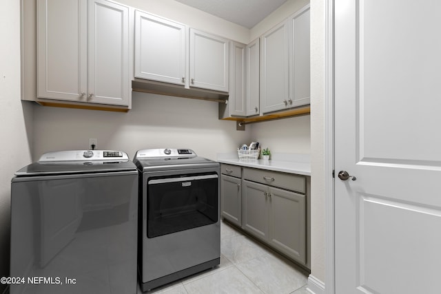 laundry area with light tile patterned flooring, washing machine and dryer, and cabinets