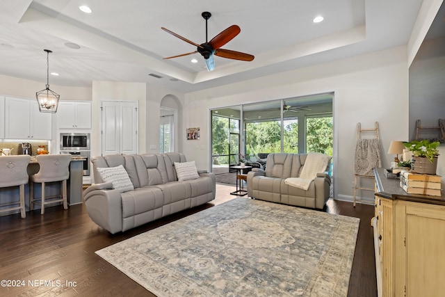 living room with dark wood-type flooring, ceiling fan with notable chandelier, a raised ceiling, and a healthy amount of sunlight