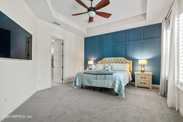 bedroom featuring light carpet, multiple windows, ceiling fan, and a raised ceiling