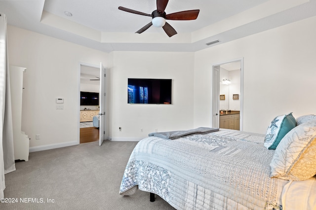 carpeted bedroom featuring ensuite bathroom, ceiling fan, and a raised ceiling