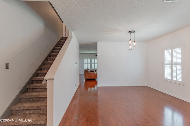 stairs featuring a notable chandelier, wood-type flooring, and a textured ceiling