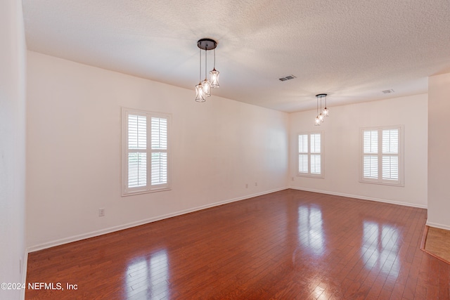 empty room featuring a notable chandelier, wood-type flooring, and a textured ceiling