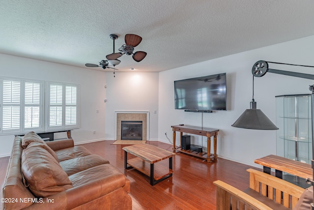 living room with ceiling fan, a textured ceiling, a tile fireplace, and wood-type flooring