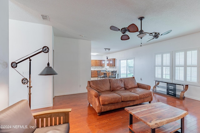 living room featuring ceiling fan, a textured ceiling, wood finished floors, visible vents, and baseboards