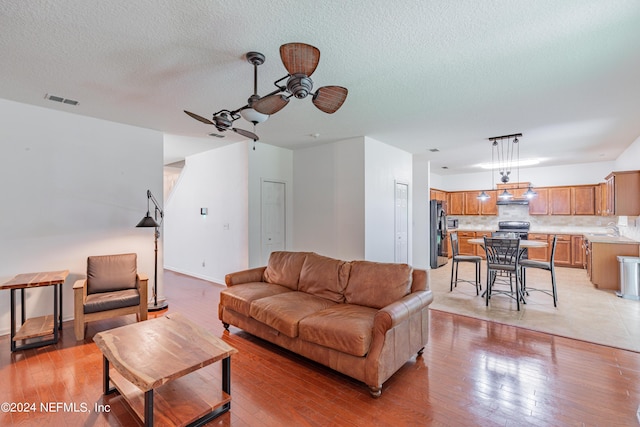 living room with a textured ceiling, a ceiling fan, visible vents, and light wood-style floors