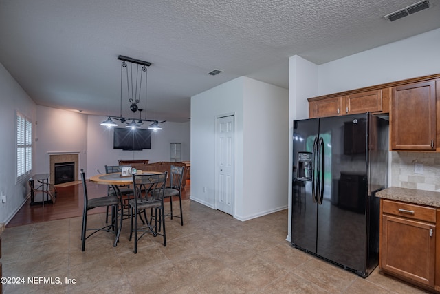 kitchen with a textured ceiling, pendant lighting, black fridge with ice dispenser, backsplash, and light wood-type flooring