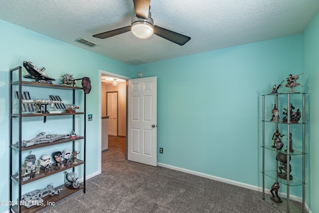 interior space featuring ceiling fan, dark carpet, and a textured ceiling