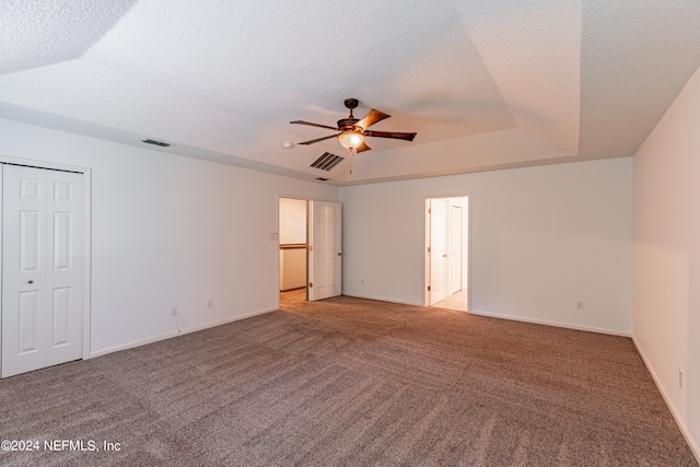 unfurnished bedroom with a textured ceiling, light colored carpet, ceiling fan, and a raised ceiling