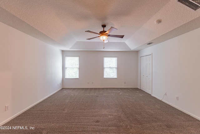 carpeted spare room with a textured ceiling, visible vents, baseboards, a ceiling fan, and a raised ceiling