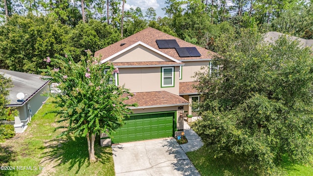 view of front of property with stucco siding, a shingled roof, an attached garage, roof mounted solar panels, and driveway