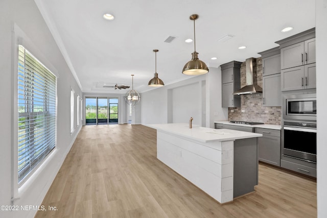 kitchen featuring appliances with stainless steel finishes, wall chimney range hood, hanging light fixtures, gray cabinets, and ceiling fan