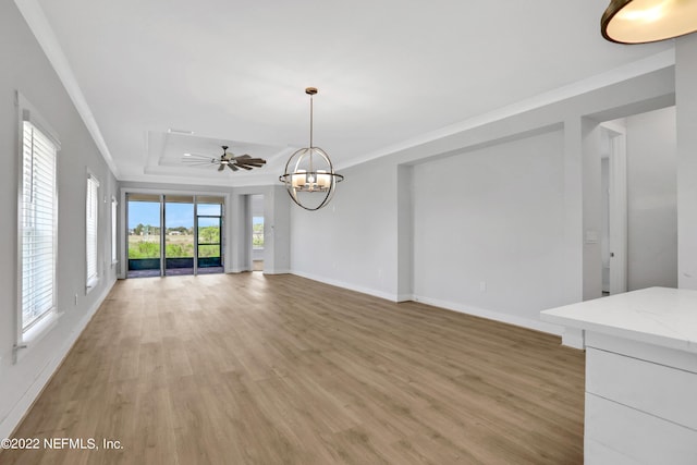 unfurnished living room featuring a raised ceiling, ceiling fan with notable chandelier, ornamental molding, and hardwood / wood-style flooring