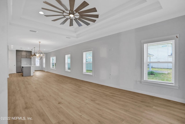 unfurnished living room with plenty of natural light, a tray ceiling, and light wood-type flooring