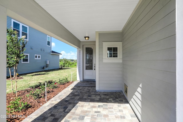 view of exterior entry featuring a lawn and a patio