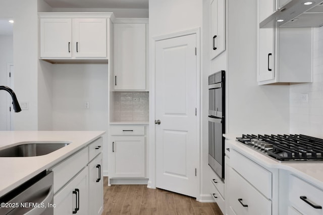 kitchen featuring sink, light wood-type flooring, stainless steel appliances, decorative backsplash, and white cabinets